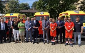 Grupa osób na czele z Marszałkiem Województwa na tle trzech ambulansów
